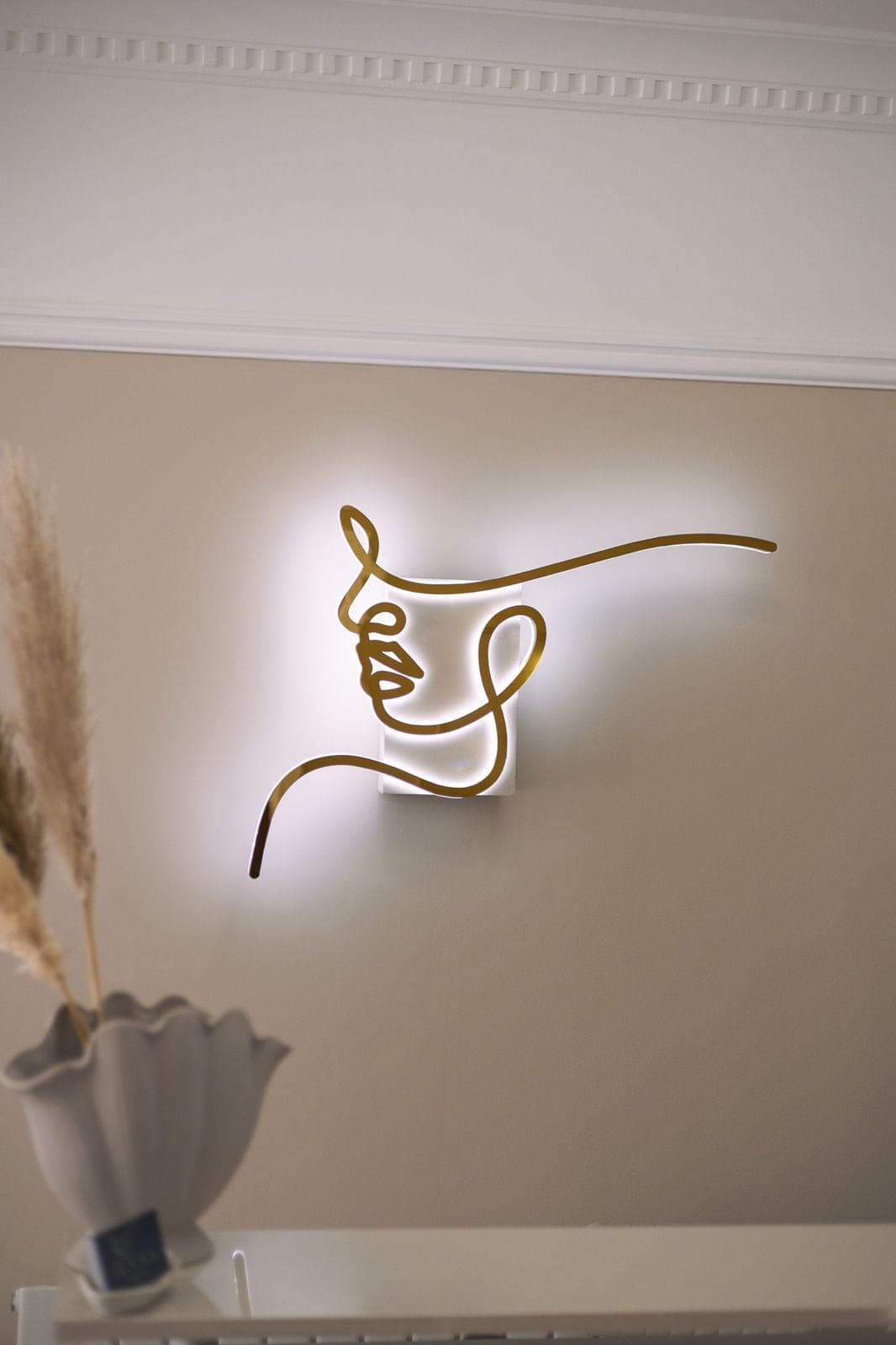 Detail of the gold line-art face sconce lit against a cream wall.