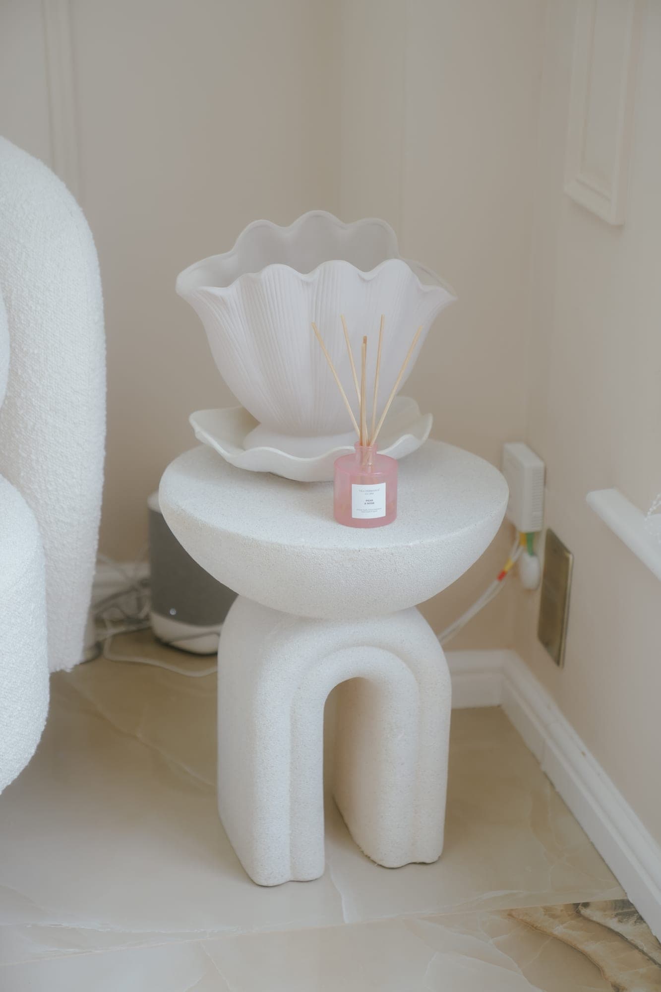 A white scalloped shell-shaped vase on a sculptural plinth side table.